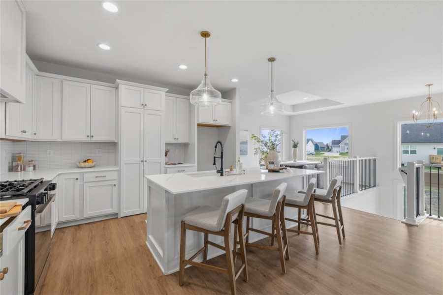 White kitchen with large island, bar stools, glass pendant lights, and staircase railing in Ankeny Iowa new home