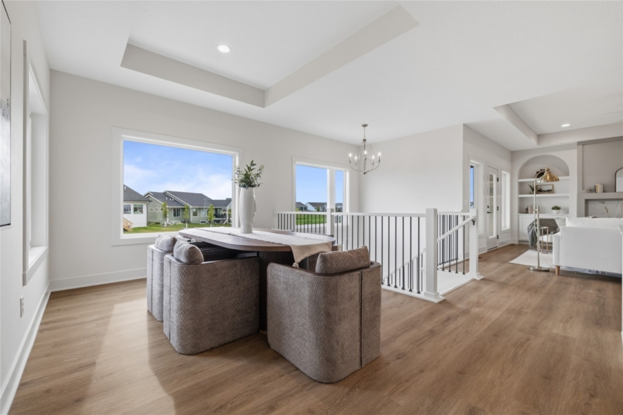 Dining area with round table, upholstered chairs, chandelier, and large windows in Ankeny Iowa new construction home
