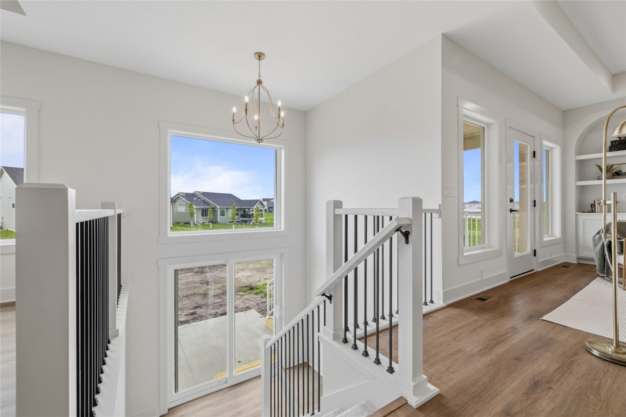 Open staircase with black iron balusters, gold chandelier, and large windows in Ankeny Iowa new build