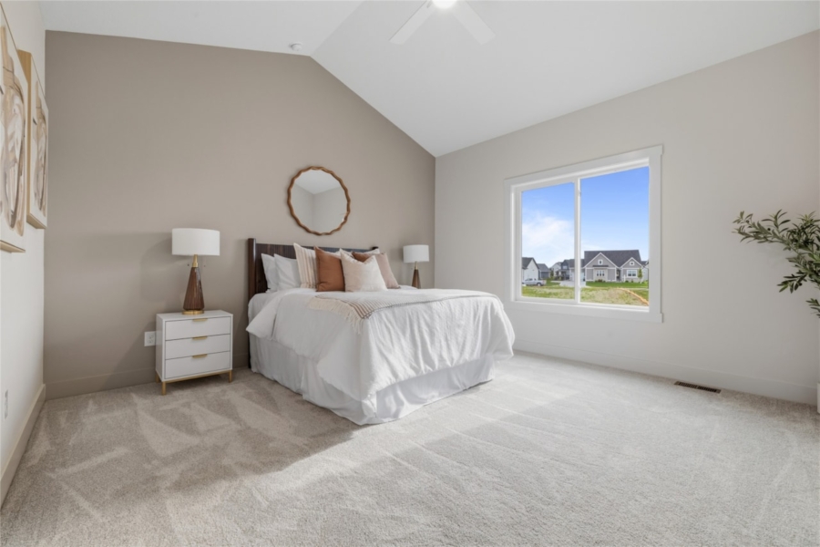 Primary bedroom with vaulted ceiling, large window, and neutral decor in Ankeny Iowa new construction home