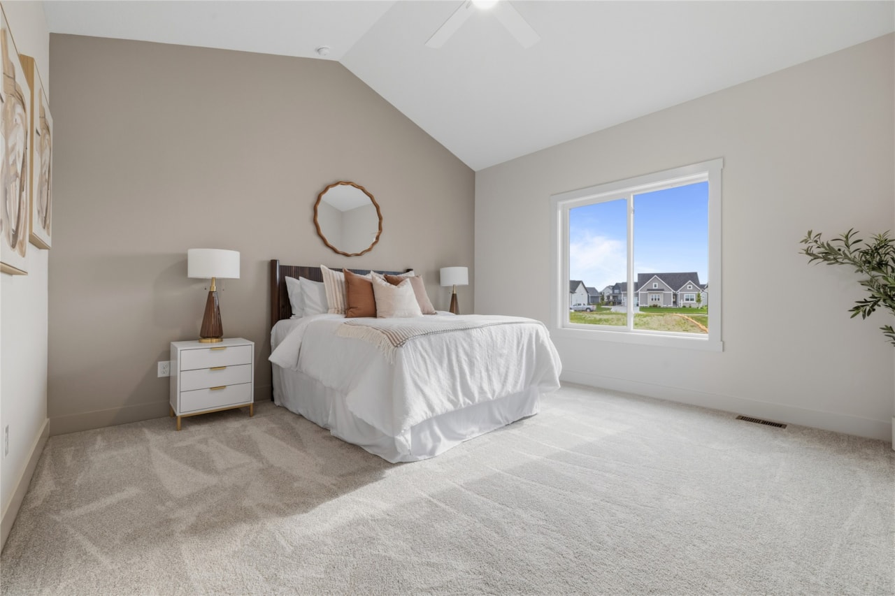 Primary bedroom with vaulted ceiling, large window, and neutral decor in Ankeny Iowa new construction home