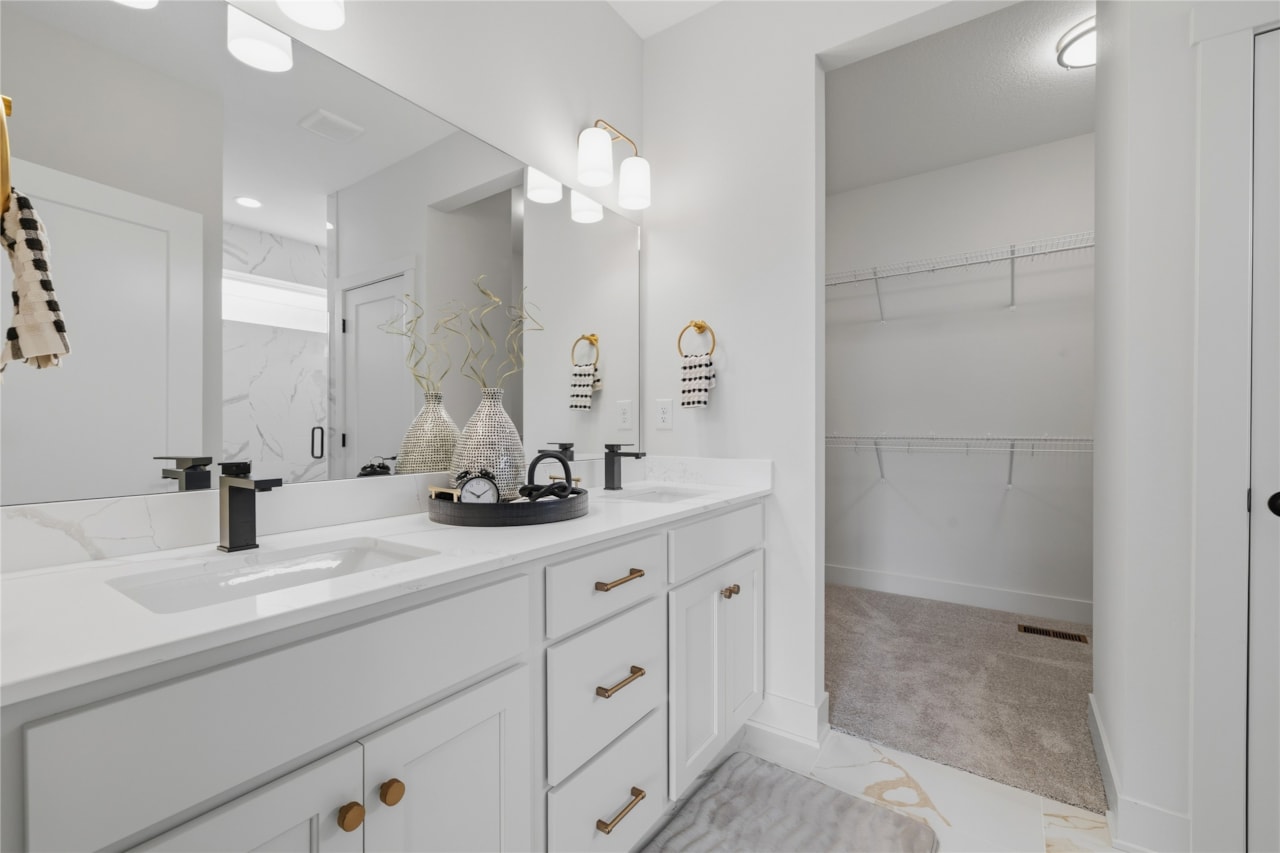 Primary bathroom with double sink vanity, gold hardware, and walk-in closet access in Ankeny Iowa new construction