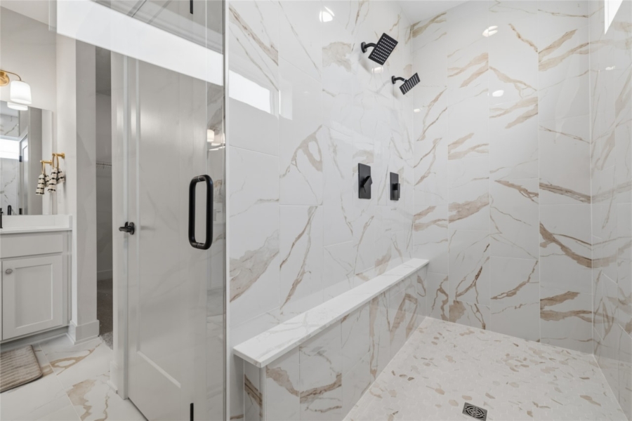Large walk-in shower with marble look tile, dual shower heads, and built-in bench in Ankeny Iowa new build