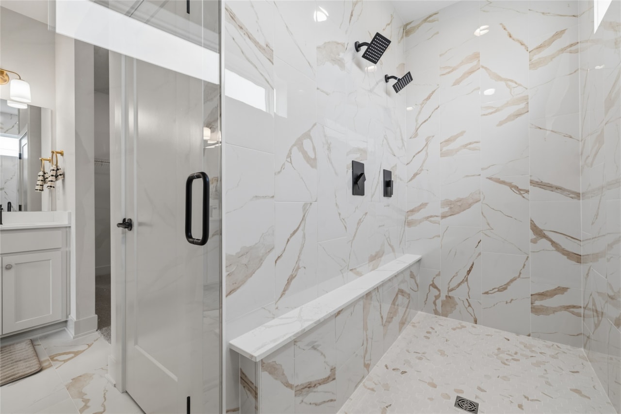 Large walk-in shower with marble look tile, dual shower heads, and built-in bench in Ankeny Iowa new build