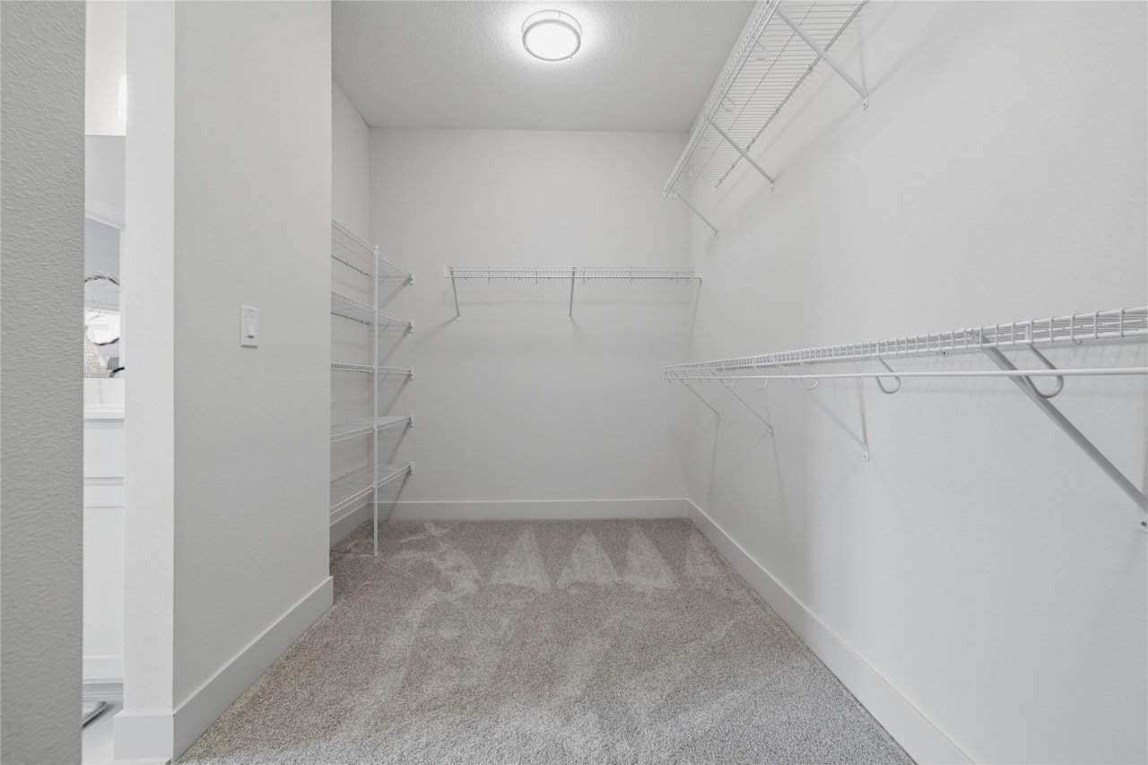 Spacious walk-in closet with white wire shelving and carpet flooring in Ankeny Iowa new home