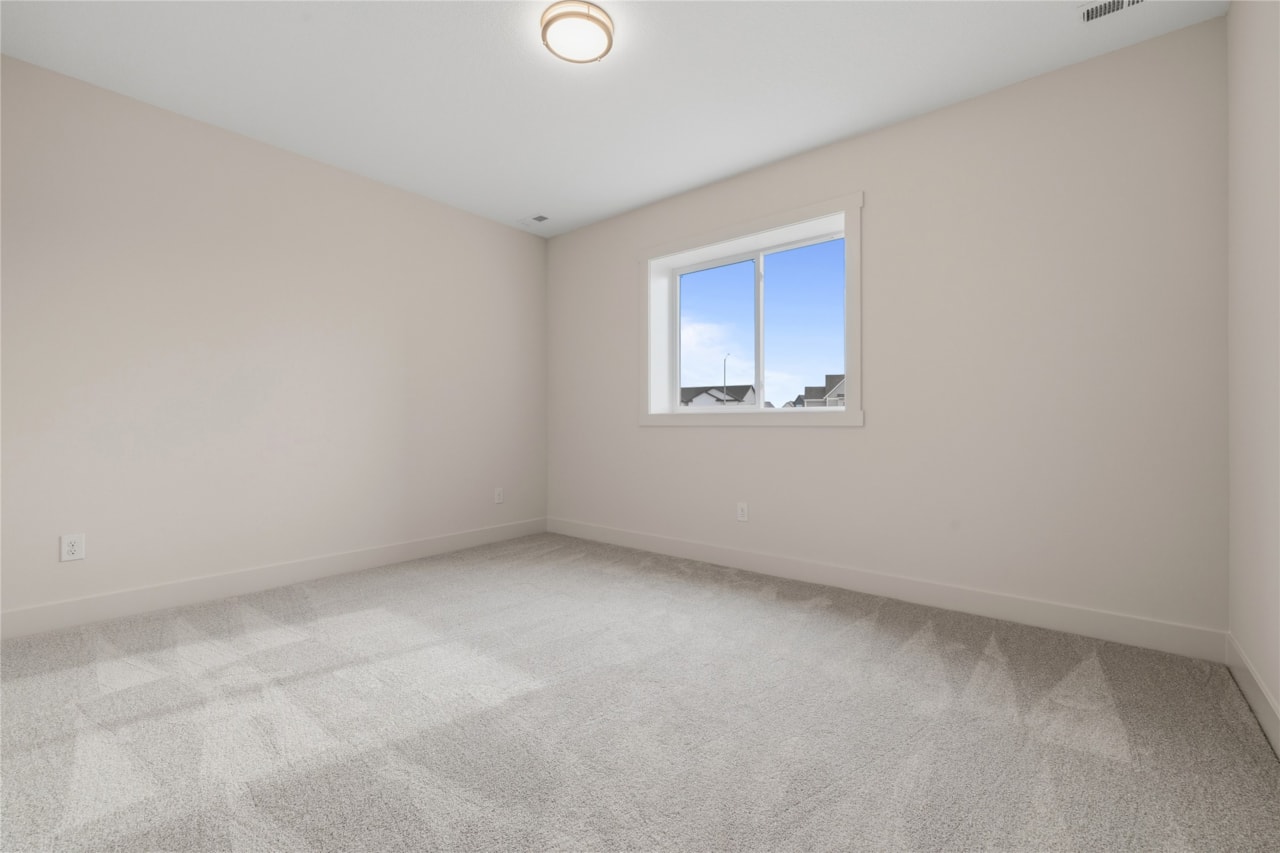Empty secondary bedroom with carpet flooring and window in Ankeny Iowa new construction home