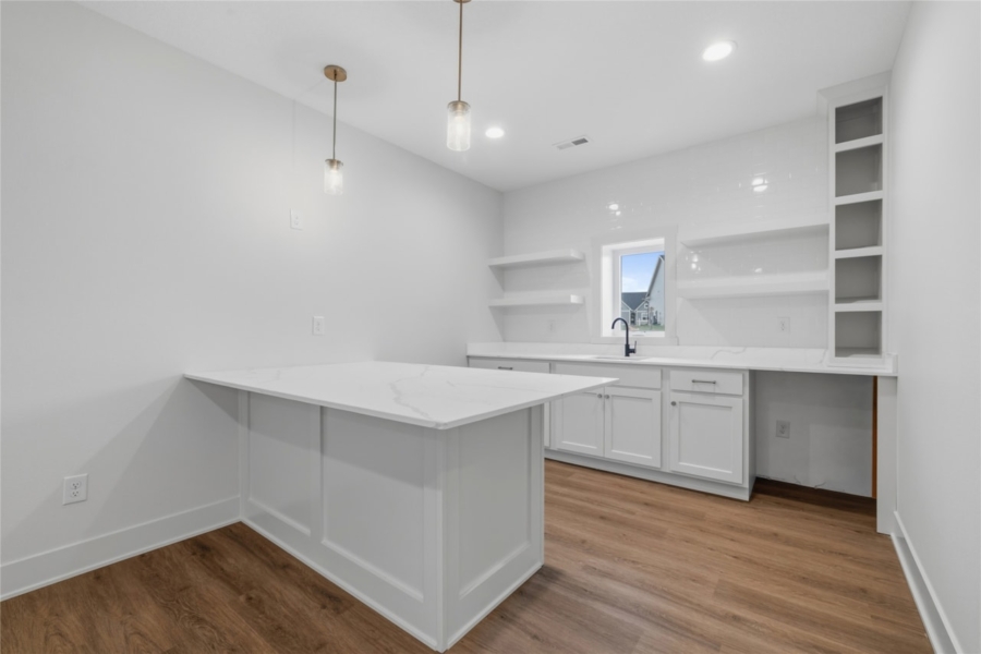 Lower level wet bar with white quartz peninsula, open shelving, white cabinets, and pendant lights in Ankeny Iowa new home