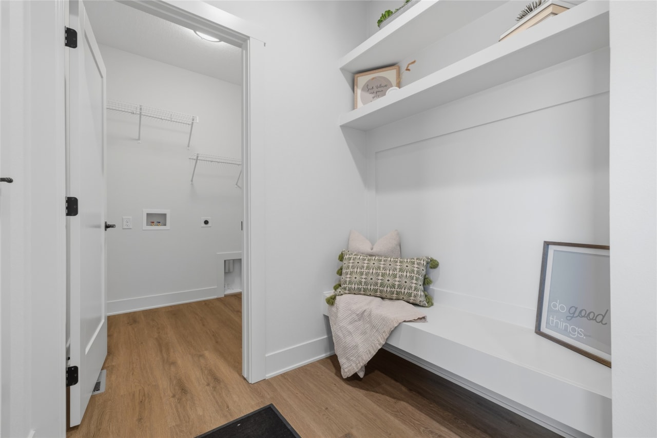 Mudroom with built-in bench, open shelving, and view into laundry room in Ankeny Iowa new construction home