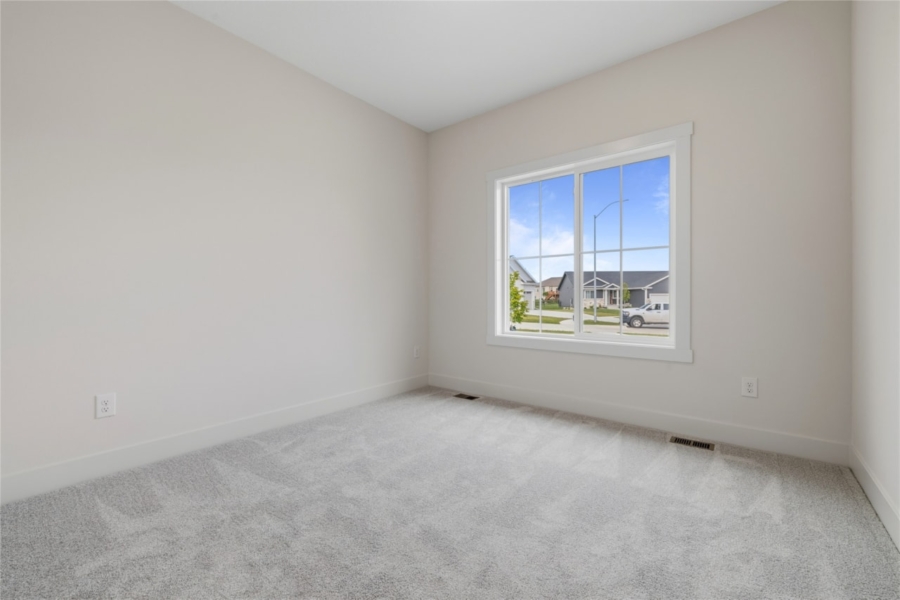 Empty main level bedroom with large triple-pane window and carpet in Ankeny Iowa new construction home