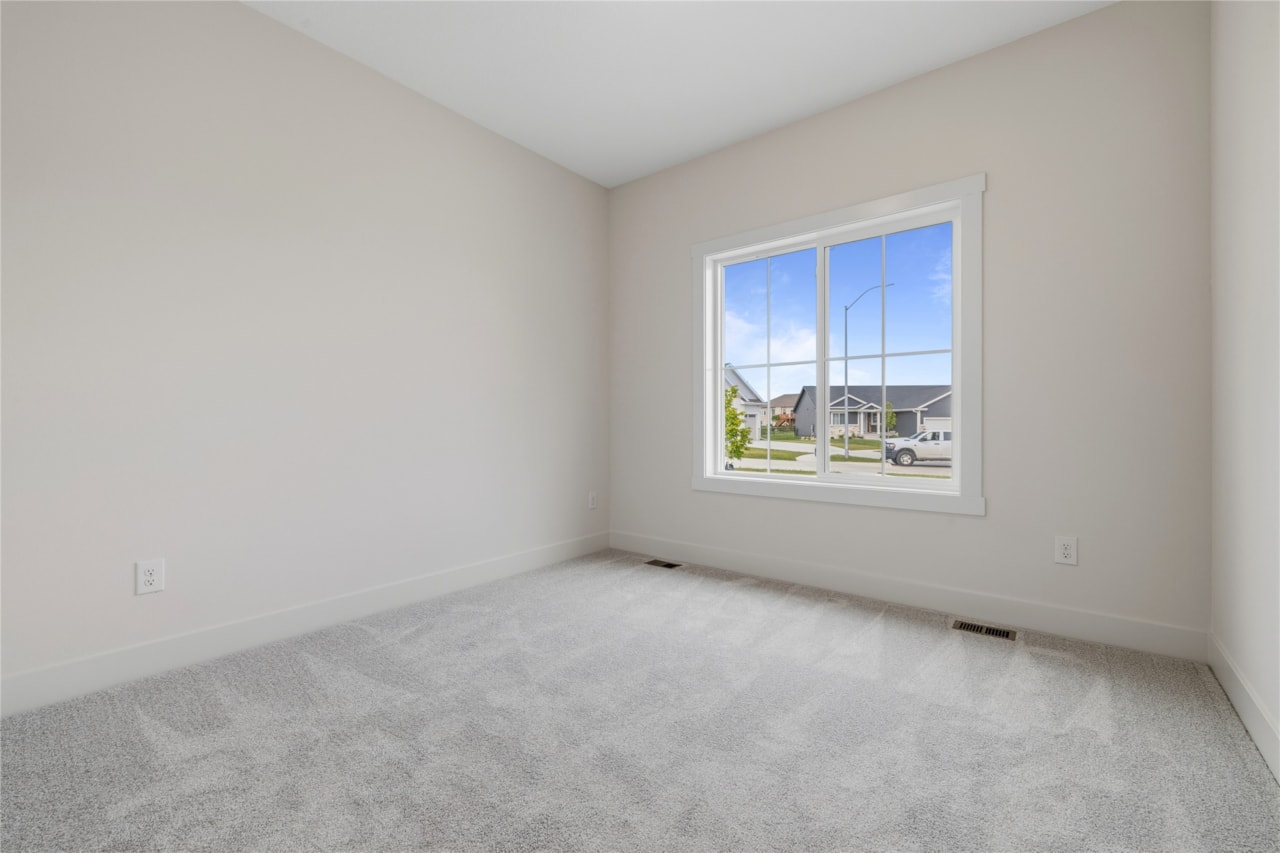 Empty main level bedroom with large triple-pane window and carpet in Ankeny Iowa new construction home