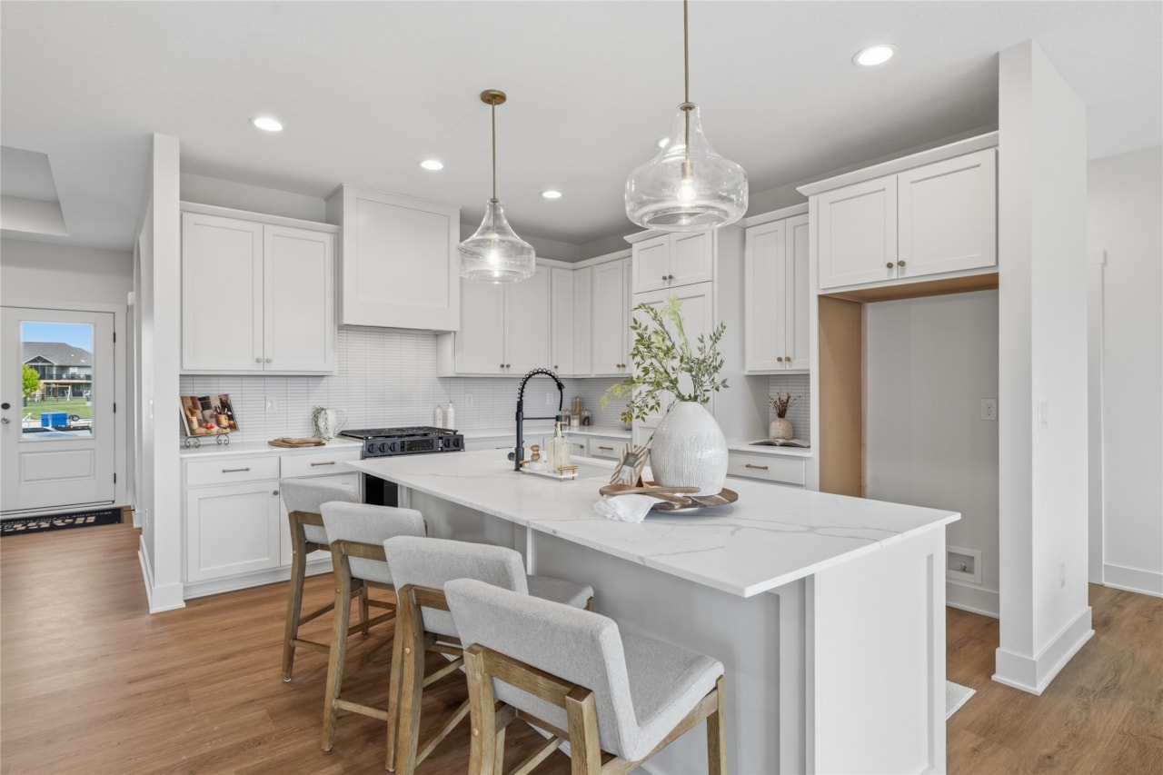 Bright white kitchen with quartz waterfall island, bar stools, and glass pendant lights in new Ankeny Iowa home