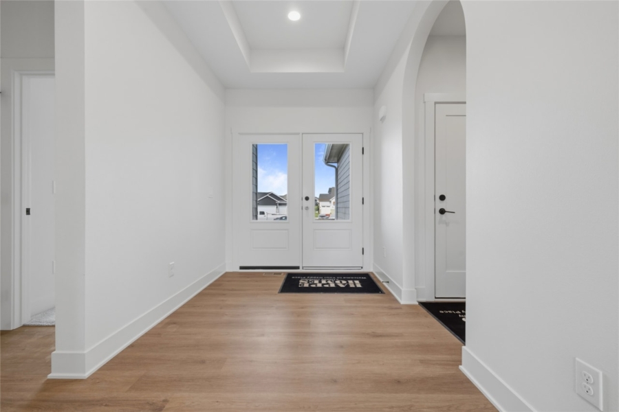 : Bright foyer entry with French-style front door, tray ceiling, arched doorway, and LVP flooring in Ankeny Iowa new construction