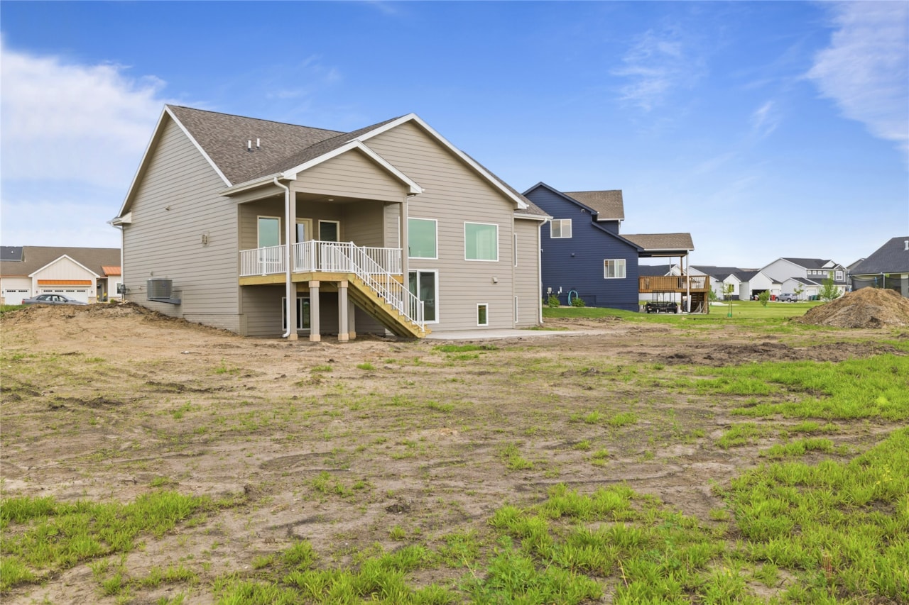 Rear Exterior with Walkout Basement and Elevated Deck – New Home in Ankeny, IA | Happe Homes Rear exterior view of new construction home with elevated deck, staircase, walkout basement, and large backyard in Ankeny Iowa