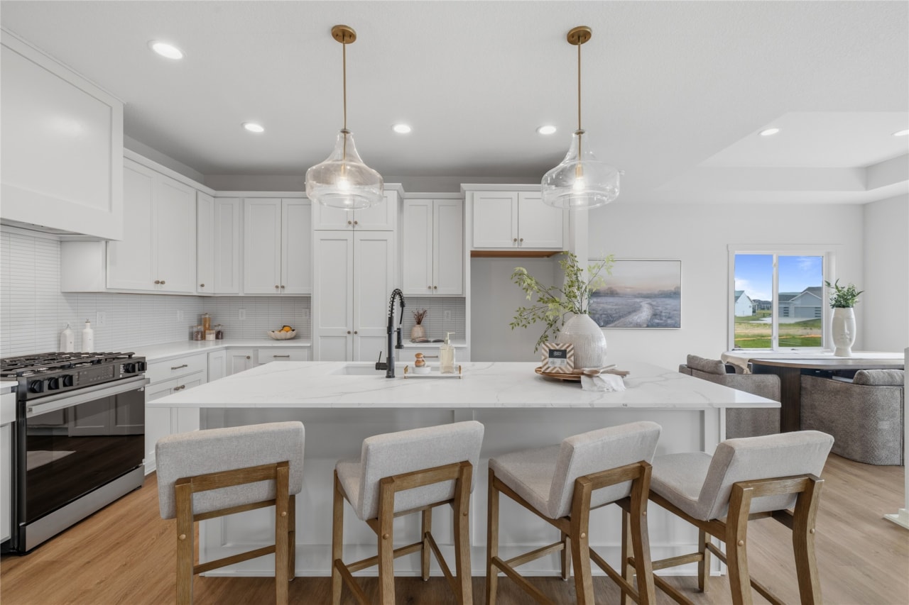 Large white quartz kitchen island with four bar stools and dual pendant lights in Ankeny Iowa new home