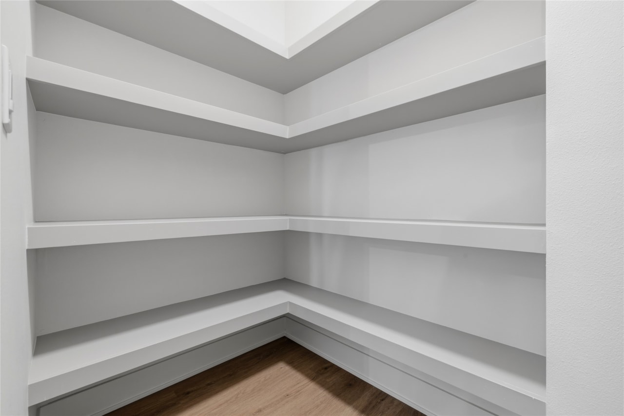 Empty walk-in pantry with white L-shaped built-in shelves and wood floor in Ankeny Iowa new home